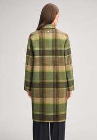 Wollkaromantel in Grün, Braun und Beige mit klassischer Silhouette. Verfügt über Seitentaschen und einen kleinen Knopfakzent am Kragen.