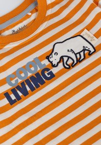 Gestreiftes Shirt in Orange und Weiß mit einem grauen Kragen, das ein Grafik eines Eisbären und den Text "COOL LIVING" in Blau und Schwarz zeigt.