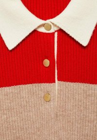 Röd och beige stickad polo tröja med vit krage, guldknappar och ett texturerat tyg med en distinkt färgblockdesign.