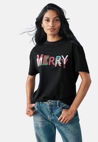 Čierne tričko s veľkým, farebným n�ápisom "MERRY" v červenej, zelenej a ružovej farbe. Krátke rukávy a voľný strih. V kombinácii s modrými džínami.