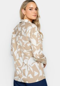 Camicia beige e bianca con motivo, colletto, maniche lunghe e vestibilità rilassata. Presenta forme astratte e un dettaglio sul retro.