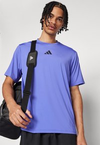 Purple athletic t-shirt made of lightweight fabric, featuring short sleeves, round neckline, and a black Adidas logo on the chest.