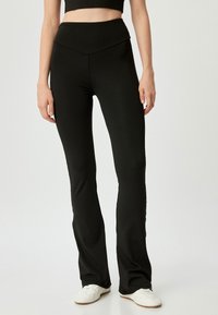 Zwarte hoogwaist flared broek van stretchy, glad materiaal, met een voorpand in V-vorm en een aansluitende pasvorm.