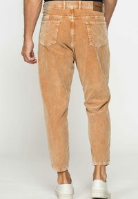 Pantaloni in corduroy marrone chiaro con gamba affusolata, dotati di tasche posteriori, superficie a trama e etichetta in vita. Abbinati a sneakers bianche.