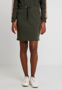 Jupe en coton mélangé vert olive avec une taille élastique à cordon, présentant des rayures latérales roses, une silhouette ajustée et une texture lisse.