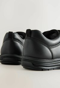 Baskets en cuir noir avec une texture lisse, une forme arrondie, des détails de couture subtils et une semelle en caoutchouc avec des rainures de traction.