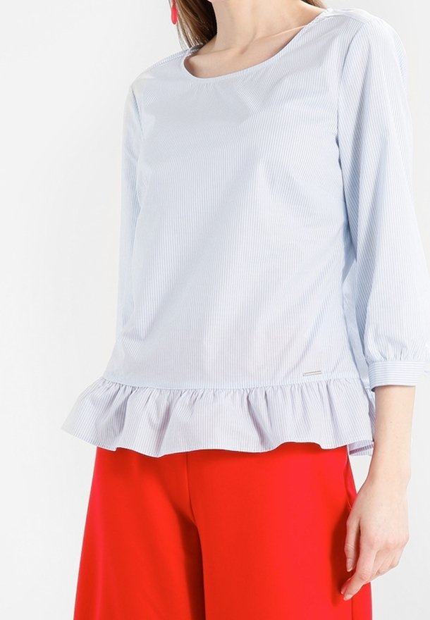 Blouse rayée bleu clair et blanche avec un col rond, des manches trois-quarts et un ourlet à volants, assortie à un pantalon large rouge vif.