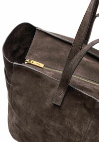 Ciemnobrązowa torba typu tote z zamszu, z skórzanymi uchwytami i złotą kieszenią na zamek błyskawiczny na zewnątrz, na białym tle.