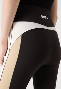 Leggings a vita alta in nero, beige e bianco. Presentano un design a blocchi di colore, una texture liscia e un logo sulla vita.