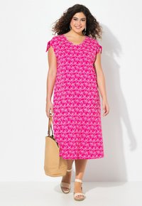 Vestido maxi de estampado floral en tonos rosa, con mangas de capucha, escote en V y acentos de lazo. Complementado con un bolso de mimbre y sandalias con tiras.