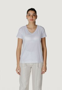T-shirt bianco a collo a V realizzato in tessuto morbido, con maniche corte e un logo discreto sul lato sinistro. Abbinato a pantaloni leggeri con fantasia.