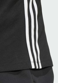 Maglietta sportiva nera con tre strisce verticali bianche lungo il lato. Realizzata in tessuto liscio, con una vestibilità regolare e dettagli di cucitura puliti.