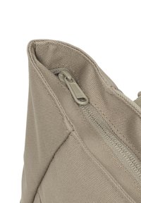 Borsa in tessuto beige con una superficie texture, che mostra un primo piano di una cerniera e punti di cucitura. Il tirante della cerniera è grigio.