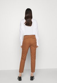 Brązowe spodnie zwężane w połączeniu z białą koszulą z długim rękawem, ukazujące gładką teksturę i minimalistyczne detale, widziane od tyłu.