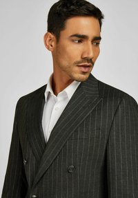 Grijs gestreepte dubbelgeknoopte blazer met twee knopen, notch revers en subtiele zakdetails, gedragen over een wit shirt.