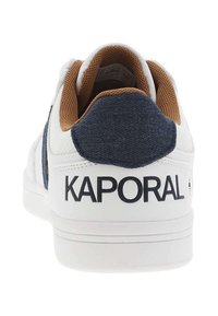 Baskets blanches avec un talon en tissu texturé, des accents marron et une marque "KAPORAL" en noir. Présente un dessus lisse et une semelle en caoutchouc.