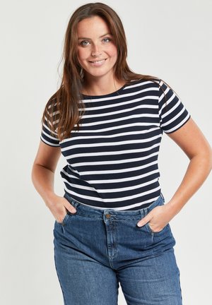 T-shirt à rayures bleu marine et blanches, à manches courtes, col rond, associé à un jean en denim bleu taille haute. Matière en coton doux.