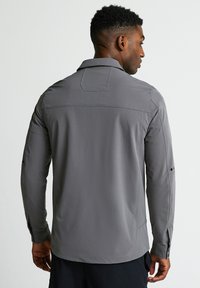 Pel�ēks garās piedurknes krekls ar apkakli, pogājamiem aprocēm, aizmugurējo vākni un gludu auduma tekstūru. Minimalistisks dizains, bez redzamām rakstām.