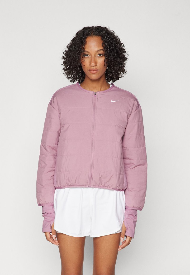 Lyserød cropped puffjakke med lynlås, rund hals og ribbede manchetter. Indeholder hvidt Nike-logo på brystet.