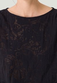Top nero con motivo floreale realizzato in tessuto leggero, presenta un colletto rotondo e una texture semitrasparente con dettagli di design intricati.