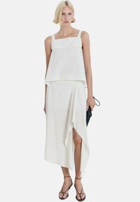 Top corto blanco a rayas con tirantes ajustables, combinado con una falda envolvente asimétrica a juego. Textura suave, diseño minimalista.