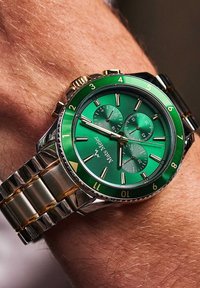 Montre chronographe verte avec un bracelet en acier inoxydable et en or jaune, dotée d'un cadran vert, d'accents dorés et de trois sous-cadrans.