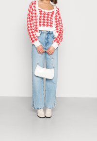 Czerwono-biały kardigan w jodełkę nałożony na biały top, w połączeniu z jasnoniebieskimi dżinsami o szerokich nogawkach i białą torebką. Całość dopełniają kremowe botki.