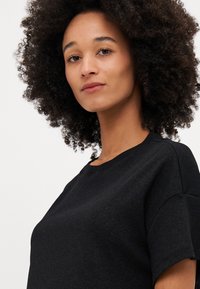 T-shirt nera in cotone con scollatura rotonda e maniche corte, caratterizzata da una consistenza morbida e una vestibilità rilassata. Design semplice senza motivi visibili.