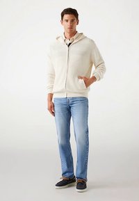 Valge soonikkoega lukuga kapuutsiga dressipluus taskuga, mis on kombineeritud helesiniste teksade ja mereväe siniste vabaajajalatsitega, mis on pruunide paeltega.