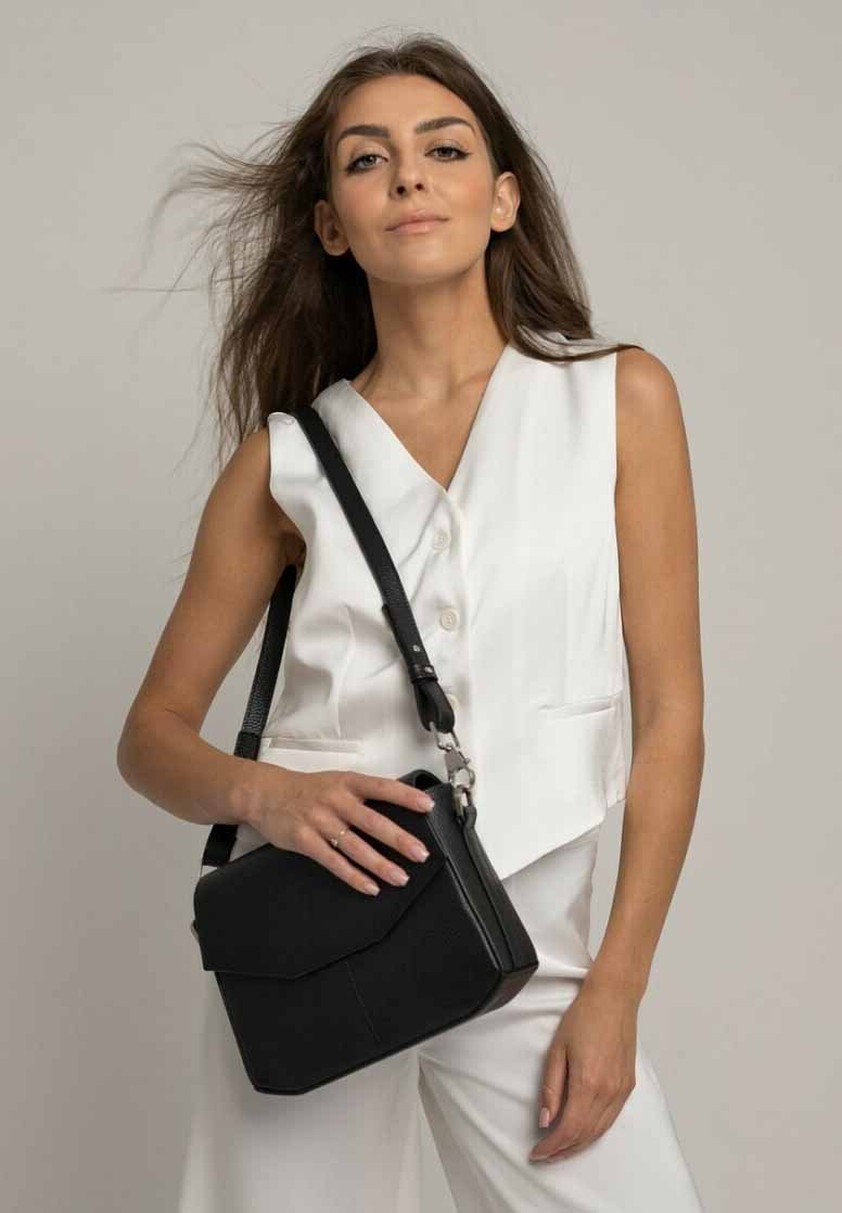 Borsa a tracolla nera in pelle con chiusura a pattina, texture morbida, design geometrico, metalli argentati e una tracolla removibile, tenuta con una mano.