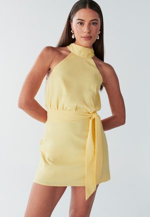 Yellow halter neck dress with a fitted waist, tie belt, and pockets. Smooth texture with a straight hem. Minimalist design.