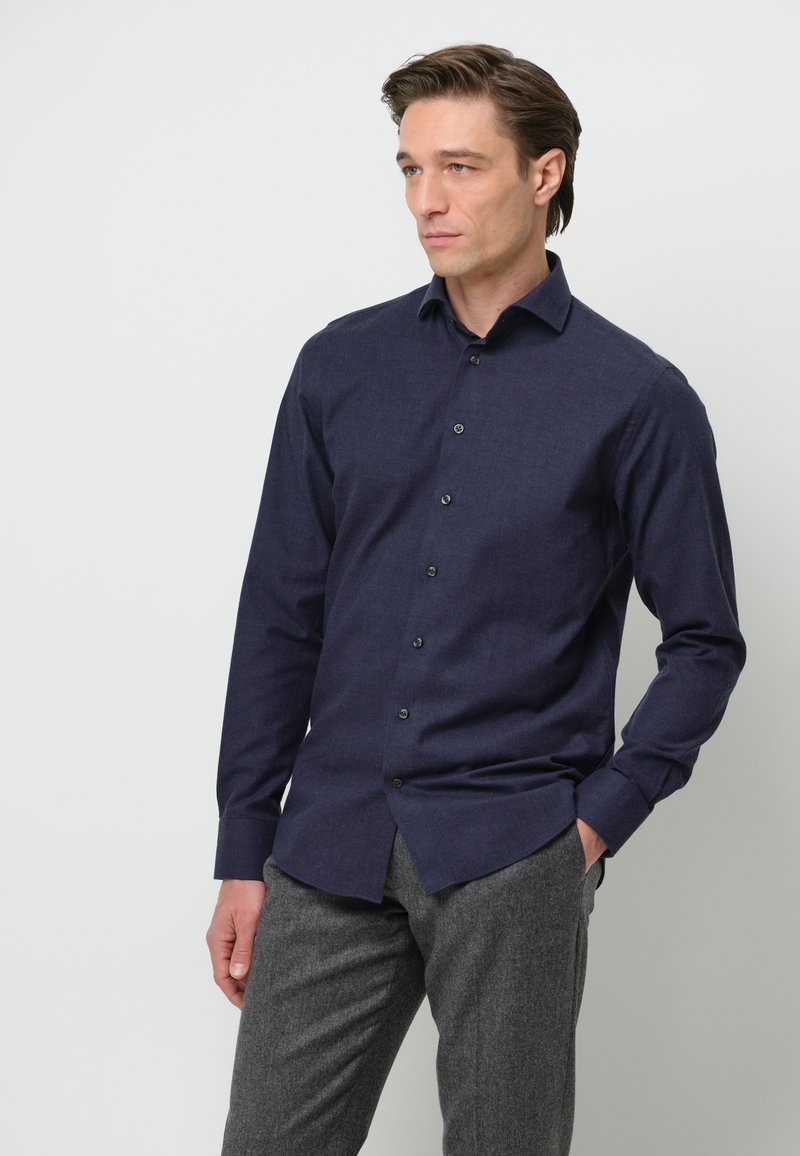 Camisa de manga larga azul marino con tejido texturizado, cuello abotonado y botones oscuros, combinada con pantalones grises texturizados.