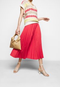 Pleated coral midi-hame yhdistettynä löysään neulottuun moniväriseen villapaitaan. Bežekäsilaukku, jossa on rusettikoristeet ja vaaleat sandaalit, joissa on remmit.