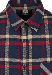 Chemise à col boutonnée avec un motif à carreaux bleu, rouge et beige, boutons noirs, et étiquette Urban Classics taille M, fabriquée en Chine.