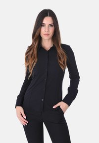 Camicia nera con bottoni, maniche lunghe, vestibilità slim, realizzata in tessuto morbido. Presenta un colletto e una chiusura a bottoni visibile lungo la parte frontale.