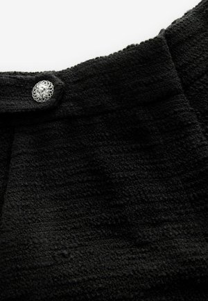 Tisă neagră cu textură, cu un model țesut și un buton decorativ argintiu cu un design floral aproape de decolteu.