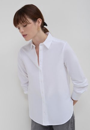 Camicia bianca con bottoni realizzata in tessuto leggero, caratterizzata da un colletto classico, maniche lunghe e orlo curvo. Senza motivi o decorazioni.