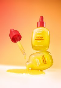 Przezroczysta żółta butelka serum z czerwoną zakrętką kroplomierza; napis brzmi "EQUAL BERRY DEEP CERA VITAMIN illuminating Serum." Ciecz wylewa się.