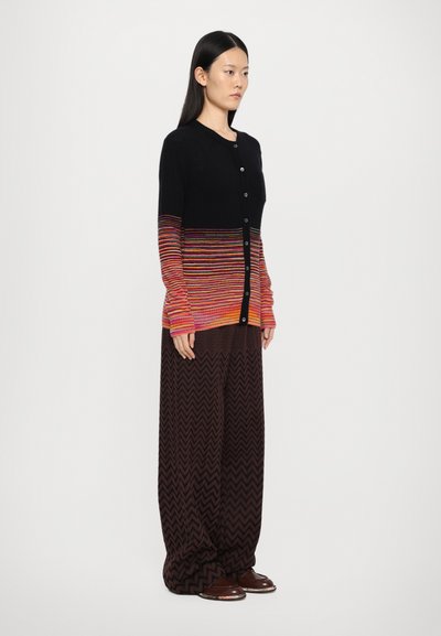 Black cardigan with vibrant striped gradient from red to yellow, featuring long sleeves and buttons, paired with brown zigzag-patterned wide pants.