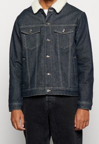 Giacca di jeans scuri con colletto in pelliccia sintetica, dotata di due tasche sul petto, tasche laterali, chiusura frontale con bottoni e dettagli di cucitura in vista.
