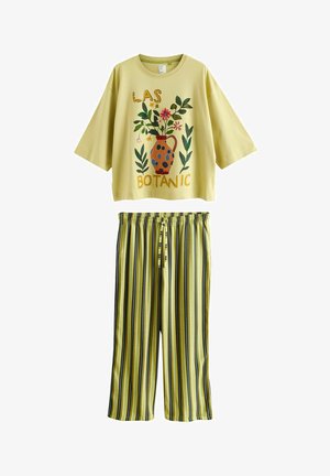 Costum galben deschis din două piese cu top cu mâneci scurte supradimensionat, având un vas floral și textul „LAS BOTANIC”, asortat cu pantaloni largi cu dungi.