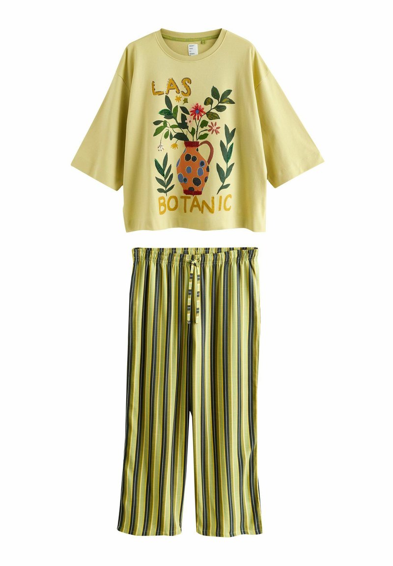 Costum galben deschis din două piese cu top cu mâneci scurte supradimensionat, având un vas floral și textul „LAS BOTANIC”, asortat cu pantaloni largi cu dungi.