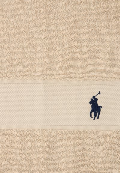 Πετσέτα σε μπεζ αποχρώσεις με υφή και ταινία με σχέδιο κηρήθρας, διακοσμημένη με κέντημα παίκτη πόλο σε σκούρο μπλε χρώμα.