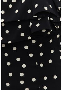 Tissu noir à pois blancs avec des détails de volants superposés.