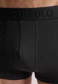 Boxer ajustados de algodón negro con una cinturilla elástica texturizada que presenta el nombre de la marca bordado, acabado suave y diseño ajustado.