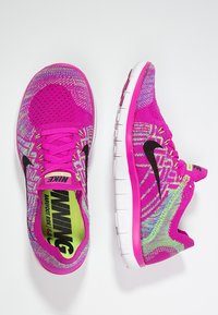 Běžecké boty Nike v jasně růžové barvě s texturovaným pleteným svrškem. Obsahují černé logo, živé zelené akcenty a flexibilní bílou podrážku.