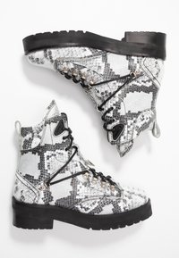 Botas de tobillo con estampado de piel de serpiente en blanco y negro, que cuentan con ganchos metálicos, un collar acolchado y una suela de goma negra gruesa.