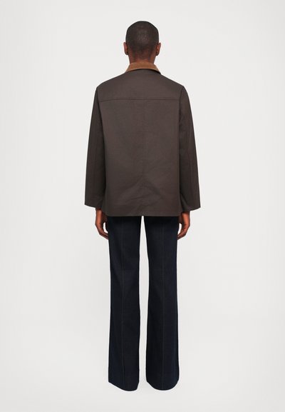 Brown jacket with a corduroy collar, straight-cut sleeves, and side slits, paired with dark blue wide-leg trousers.