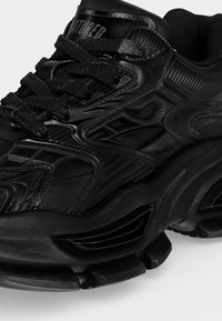 Μαύρο chunky sneaker με υφασμάτινες λεπτομέρειες, παχύ πάτο και μαύρα κορδόνια, σε προβολή από εμπρός και πλευρικά σε απλό φόντο.