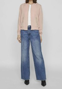 Light pink bomber jacket with zip pockets, paired with high-waisted, wide-leg blue jeans. Black heeled shoes complete the outfit.